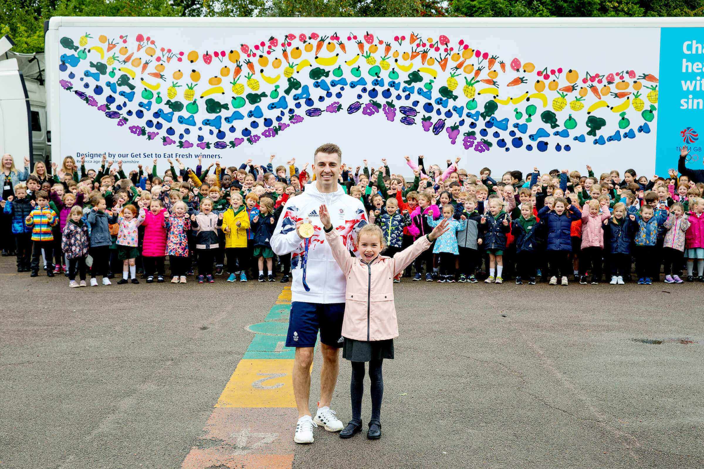 Max Whitlock with Design a Lorry winner Rebecca in front of her lorry and cheering classmates.