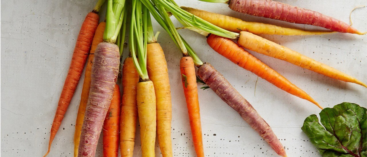 Yellow, orange and purple carrots with green leaves on a chopping board.