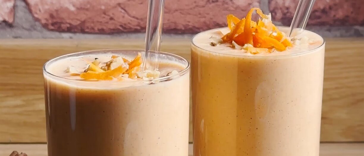 Two glasses of carrot cake smoothie, a terracotta coloured liquid, with carrot shavings on top. 